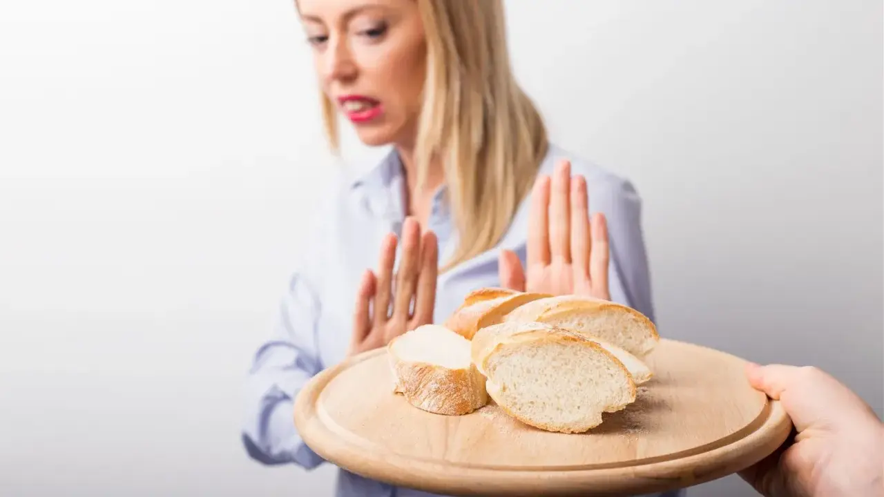 Kobieta z przerażeniem odrzuca talerz z kromkami chleba. Jej gesty sugerują uczulenie na chleb lub nietolerancję glutenu.