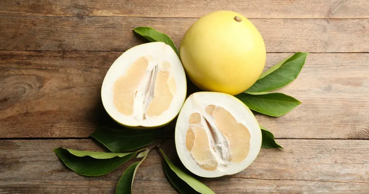 Całe i przekrojone pomelo na drewnianym tle. Czy pomelo jest zdrowe? Tak, to pyszny i odżywczy owoc.