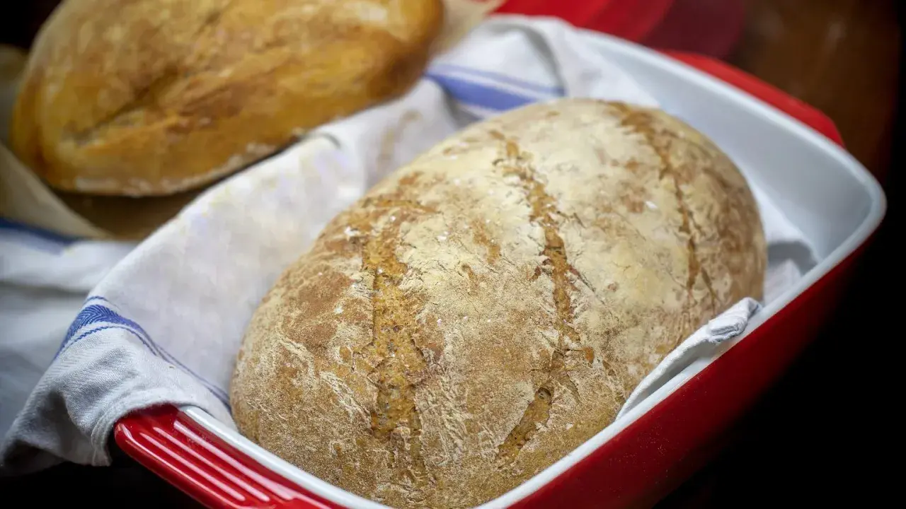 Dwa bochenki chleba bez drożdży w czerwonej formie, jeden na drugim, na białym ręczniku z niebieskimi paskami.