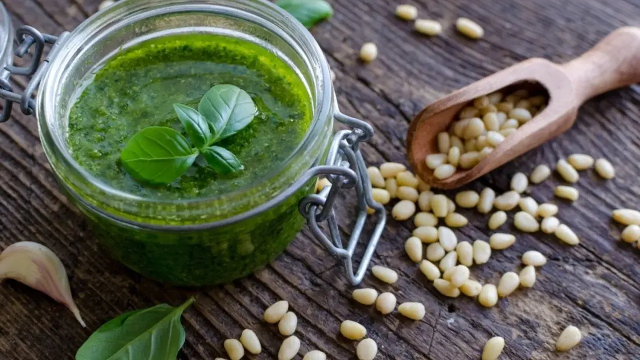Słoik domowego pesto, świeża bazylia, czosnek i orzeszki piniowe na drewnianym blacie. Pesto co to? To aromatyczny sos idealny do makaronu.
