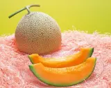 Cały melon i dwa kawałki soczystego, pomarańczowego miąższu na różowym tle. Czy to najdroższy owoc świata?
