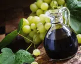 Ciemny ocet winny w karafce obok kiści zielonych winogron. Dowiedz się, jak pić ocet winny dla zdrowia.