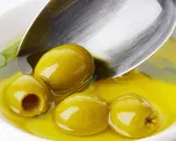 Zielone oliwki w złocistej oliwie, łyżka sugeruje porcję. Ile pić oliwy z oliwek dziennie?
