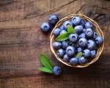 Koszyk pełen borówek na drewnianym tle. Zastanawiasz się, ile kcal mają borówki? Są niskokaloryczne i pełne witamin!