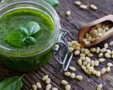 Słoik domowego pesto, świeża bazylia, czosnek i orzeszki piniowe na drewnianym blacie. Pesto co to? To aromatyczny sos idealny do makaronu.