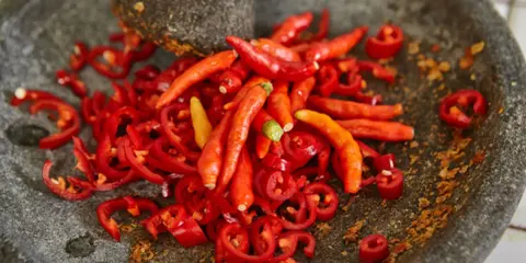 Kawałki i całe papryczki chili w moździerzu. Przygotowanie najostrzejszego jedzenia na świecie.
