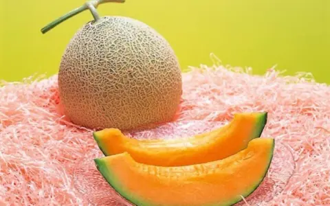 Cały melon i dwa kawałki soczystego, pomarańczowego miąższu na różowym tle. Czy to najdroższy owoc świata?