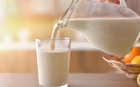 Mleko bez laktozy nalewane do szklanki. Czy mleko bez laktozy jest zdrowe? Obok koszyk z owocami cytrusowymi.
