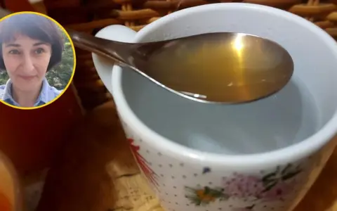 Kobieta z uśmiechem na twarzy pokazuje łyżkę z płynem, który wygląda jak ocet jabłkowy, gotowy do dodania do wody w kubku.