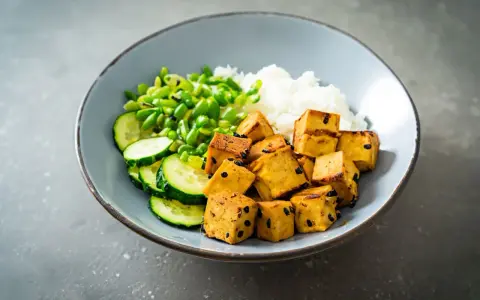 Misternie pokrojone kostki tofu, które nie zawierają glutenu, podane z ryżem, ogórkiem i zielonym groszkiem.