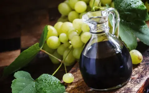 Ciemny ocet winny w karafce obok kiści zielonych winogron. Dowiedz się, jak pić ocet winny dla zdrowia.
