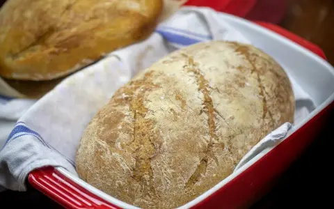 Dwa bochenki chleba bez drożdży w czerwonej formie, jeden na drugim, na białym ręczniku z niebieskimi paskami.