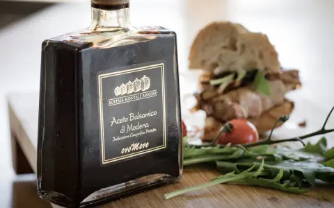 Butelka octu balsamicznego z Modeny obok kanapki i rukoli. Ocet winny i balsamiczny to dwa różne smaki.