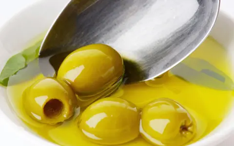 Zielone oliwki w złocistej oliwie, łyżka sugeruje porcję. Ile pić oliwy z oliwek dziennie?