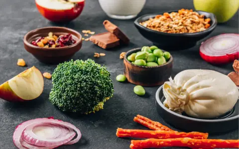 Składniki na dietę dr Budwig: brokuły, fasolka edamame, twaróg, jabłka, cebula, granola, suszone owoce, czekolada.