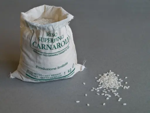 Worek z ryżem Carnaroli, idealnym do risotto. Kilka ziaren rozsypanych obok.