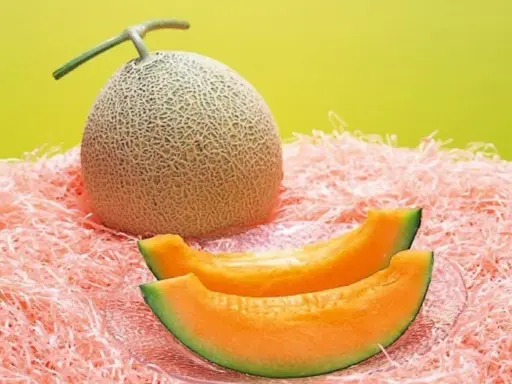 Cały melon i dwa kawałki soczystego, pomarańczowego miąższu na różowym tle. Czy to najdroższy owoc świata?