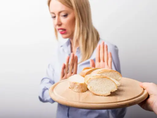 Kobieta z przerażeniem odrzuca talerz z kromkami chleba. Jej gesty sugerują uczulenie na chleb lub nietolerancję glutenu.