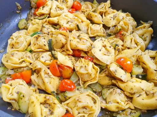 Jak ugotować tortellini z cukinią i pomidorkami koktajlowymi. Danie wygląda apetycznie i jest gotowe do podania.