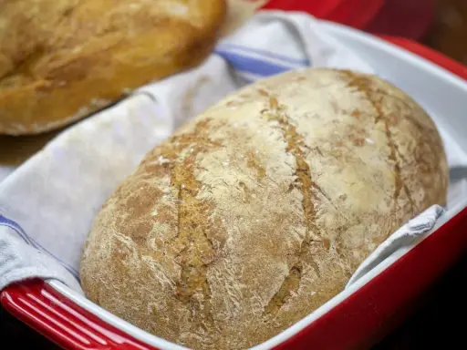 Dwa bochenki chleba bez drożdży w czerwonej formie, jeden na drugim, na białym ręczniku z niebieskimi paskami.