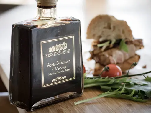 Butelka octu balsamicznego z Modeny obok kanapki i rukoli. Ocet winny i balsamiczny to dwa różne smaki.