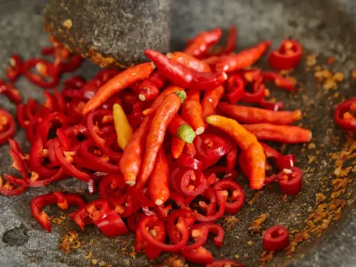 Kawałki i całe papryczki chili w moździerzu. Przygotowanie najostrzejszego jedzenia na świecie.