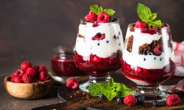 Pyszne fit desery bez pieczenia z malinami, borówkami i bitą śmietaną w szklanych pucharkach.