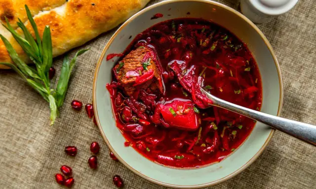 A miseczka sycącego barszczu czerwonego z kawałkiem mięsa, obok pieczywo i ziarna granatu. Czy barszcz czerwony jest zdrowy? Tak, to bogactwo witamin!