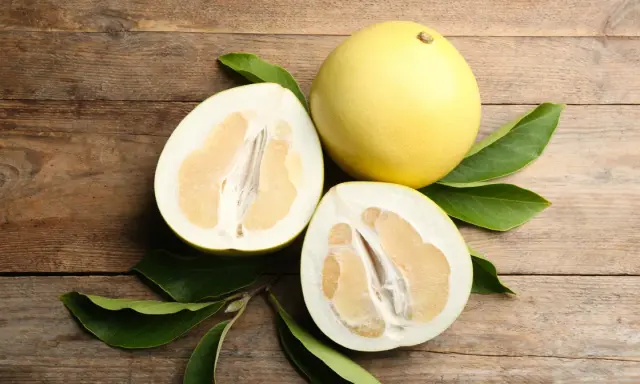 Całe i przekrojone pomelo na drewnianym tle. Czy pomelo jest zdrowe? Tak, to pyszny i odżywczy owoc.