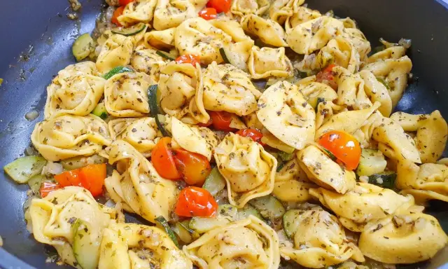 Jak ugotować tortellini z cukinią i pomidorkami koktajlowymi. Danie wygląda apetycznie i jest gotowe do podania.
