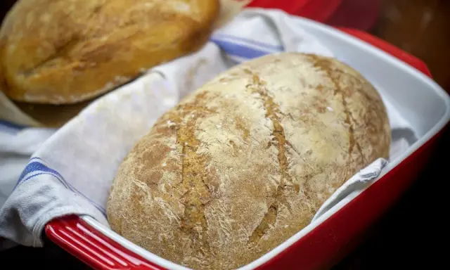 Dwa bochenki chleba bez drożdży w czerwonej formie, jeden na drugim, na białym ręczniku z niebieskimi paskami.