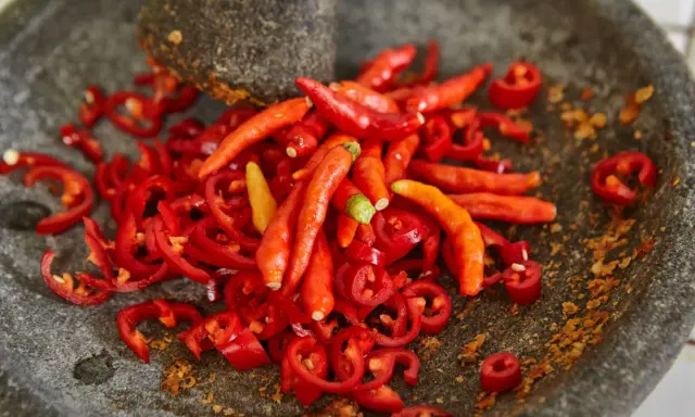 Kawałki i całe papryczki chili w moździerzu. Przygotowanie najostrzejszego jedzenia na świecie.