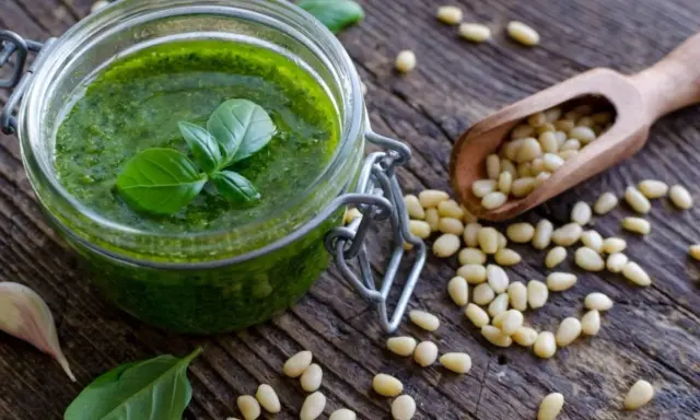 Słoik domowego pesto, świeża bazylia, czosnek i orzeszki piniowe na drewnianym blacie. Pesto co to? To aromatyczny sos idealny do makaronu.