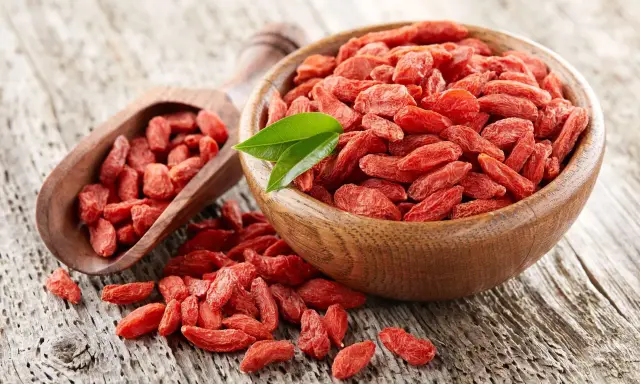 Suszone jagody goji w drewnianej misce i łopatce. Uważaj na jagody goji skutki uboczne, choć są zdrowe, mogą wchodzić w interakcje z lekami.
