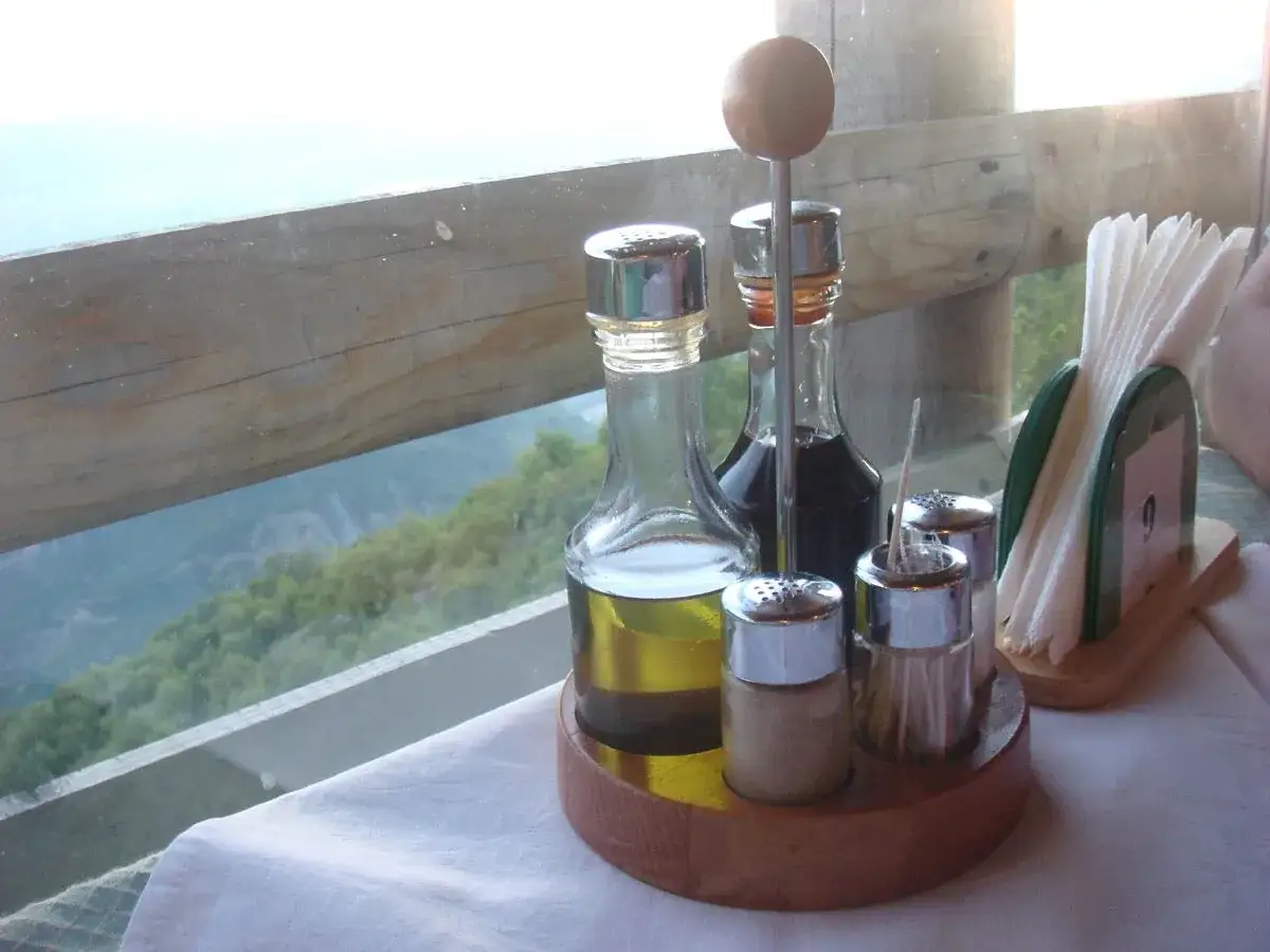 Zestaw do przypraw: oliwa, ocet winny i balsamiczny, solniczka i pieprzniczka na drewnianej podstawce.