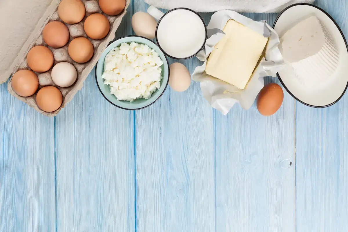 Jaki nabiał na keto? Jajka, twar&oacute;g, masło i mleko na niebieskim drewnianym tle. Idealne składniki na dietę ketogeniczną.