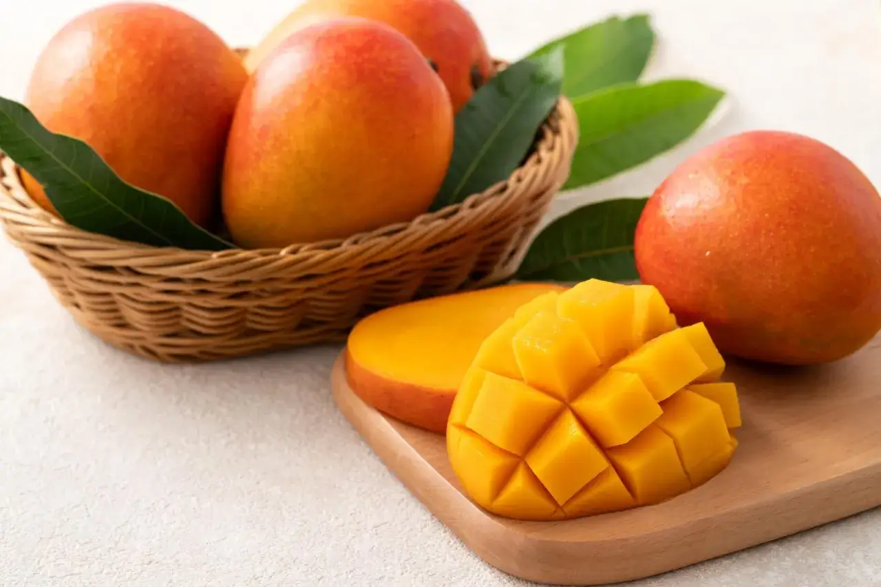 Koszyk pełen dojrzałych mango i pokrojony owoc na desce. Czy mango indeks glikemiczny jest niski?