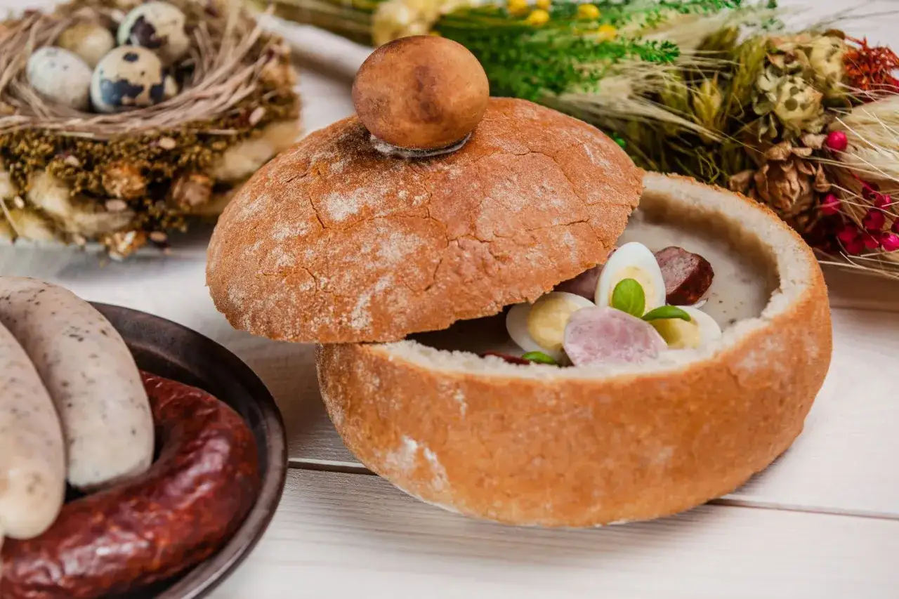 Tradycyjne obiady jak u babci przepisy: żurek w chlebie z kiełbasą i jajkiem, obok biała kiełbasa i jajka przepi&oacute;rcze w gnieździe.