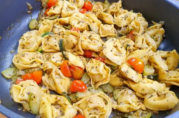 Jak ugotować tortellini z cukinią i pomidorkami koktajlowymi. Danie wygląda apetycznie i jest gotowe do podania.